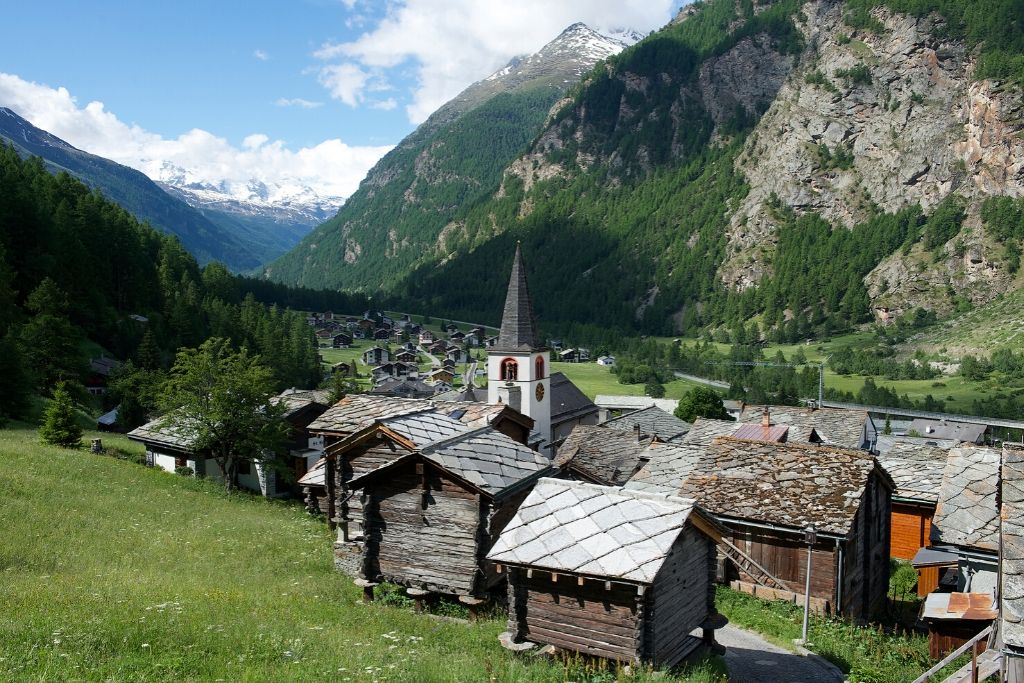 Aussicht über Randa mit Kirche und kleinen Holzhäusern. Im Hintergrund ragen die Berge umhoch