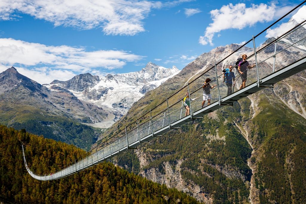 Vier Wanderer laufen über die lange Hängebrücke, die sich über das Tal spannt